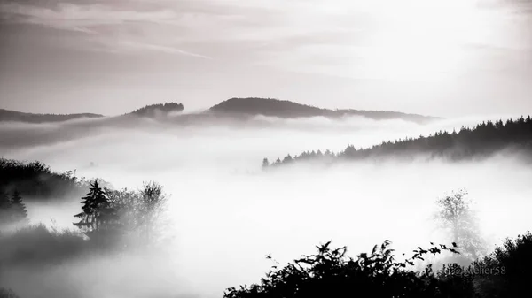 Black and white shot of mountains in fog under a cloudy sky — Stock Photo, Image