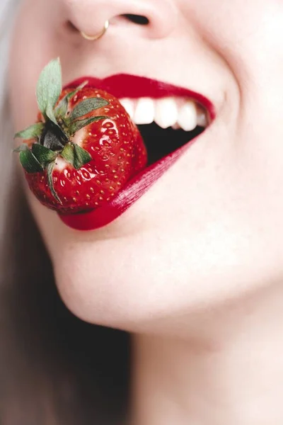 用红色口红咬草莓的年轻女性的垂直特写照片 — 图库照片