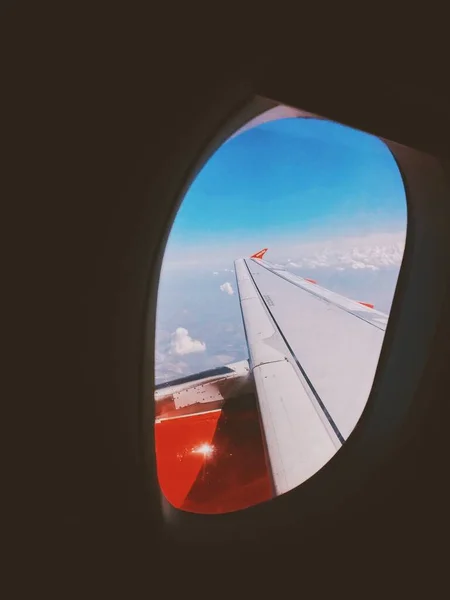 Un gros plan des ailes de l'avion montré à travers la fenêtre avec de beaux nuages en arrière-plan — Photo