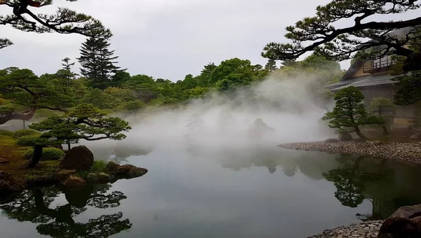 Hermosa toma de una casa cerca del agua y árboles en una niebla — Foto de Stock