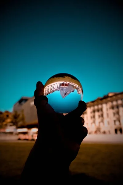 Una persona sosteniendo una bola de vidrio con el reflejo de los edificios y el cielo azul —  Fotos de Stock