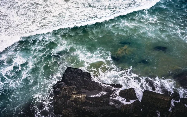 Boven foto van een rotsachtige kust in de buurt van een lichaam van water met rotsen spatten op de rotsen — Stockfoto