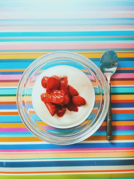 Йогурт у скляній мисці з полуницею зверху біля срібної ложки на барвистій смугастій поверхні — стокове фото