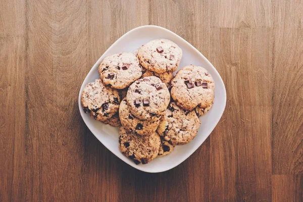 Primer plano de alto ángulo de deliciosas galletas de chocolate en un plato blanco en una mesa de madera —  Fotos de Stock