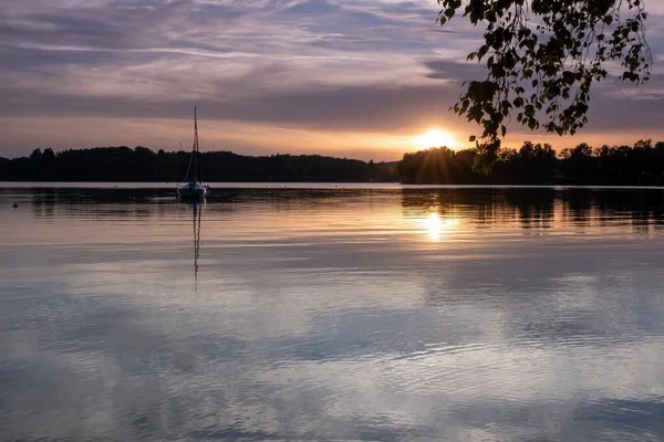 Båt seglar på vattnet med en skog i fjärran under en molnig himmel — Stockfoto