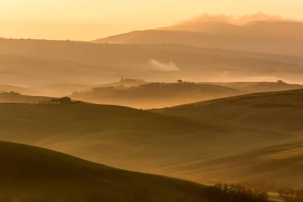 Horizontal shot of a lot of green hills covered with fog in the evening — Stock Photo, Image