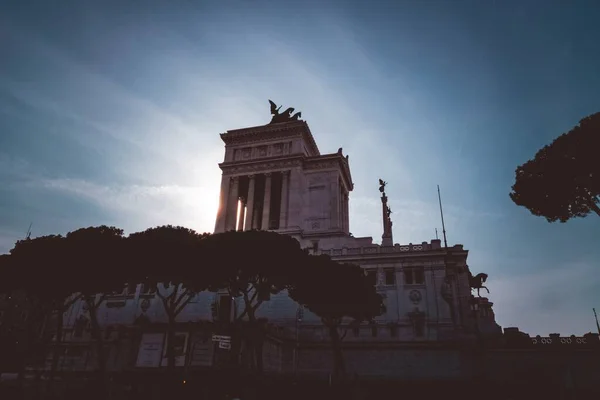 Horizontal low angle shot of ancient Roman architecture surrounded by green trees during sunset — ストック写真