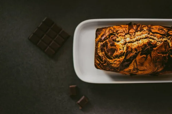 Υψηλής γωνίας βολή κέικ σοκολάτας σε λευκό πιάτο δίπλα σε μπάρες σοκολάτας σε ξύλινη επιφάνεια — Φωτογραφία Αρχείου