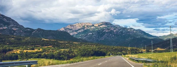 Панорамный снимок трассы, проходящей через горную долину с густыми облаками, собирающимися в небе — стоковое фото