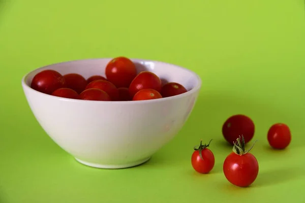 Nahaufnahme kleiner roter Tomaten in einer weißen Schüssel und auf einer grünen Oberfläche — Stockfoto