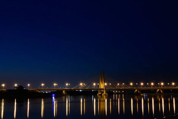 Amplio plano de un puente sobre el agua con el reflejo de luces bajo el hermoso cielo nocturno — Foto de Stock