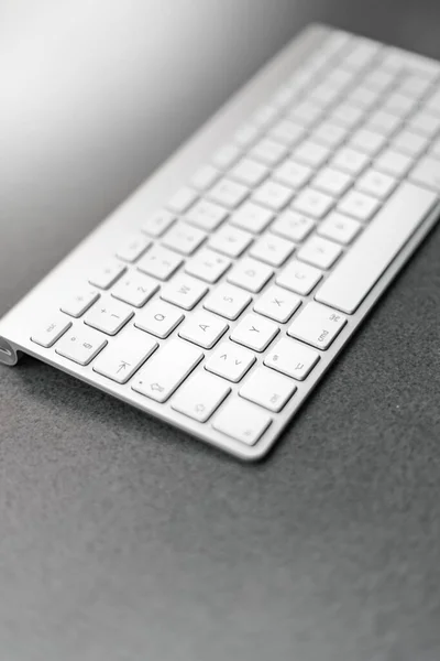 Vertikale Graustufenaufnahme einer weißen Tastatur auf einer grauen Oberfläche — Stockfoto