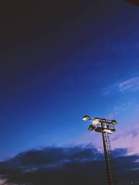 Vertical tiro de ângulo baixo de uma torre de luz sob o céu azul nublado à noite — Fotografia de Stock
