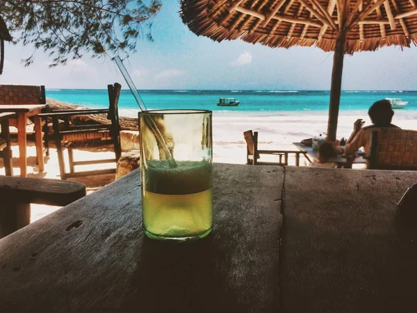 Primer plano de una taza de vidrio transparente llena de jugo en la playa con el hermoso mar —  Fotos de Stock