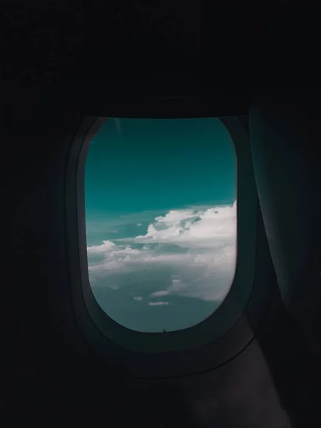 Tiro vertical de uma janela de avião com a visão de nuvens e um céu azul escuro — Fotografia de Stock