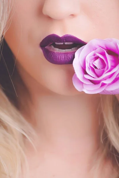 Close-up shot van een vrouw met paarse lippenstift met roze roos dicht bij haar lippen — Stockfoto