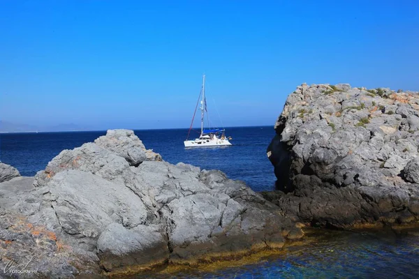 Hermoso tiro de las rocas cerca de un cuerpo de agua con un yate blanco navegando a distancia. —  Fotos de Stock