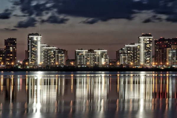 Amplio plano de hermosos edificios de gran altura cerca del agua bajo el cielo nublado por la noche —  Fotos de Stock