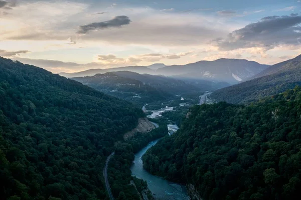 Hoge hoek shot van een rivier in het midden van beboste bergen onder een bewolkte lucht — Stockfoto