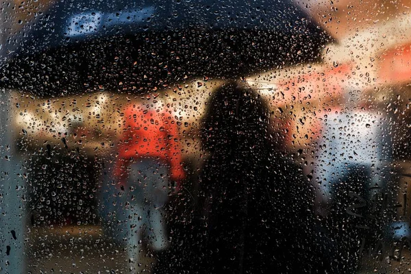 Foto horizontal de personas sosteniendo paraguas en la noche detrás del vidrio cubierto con gotas de lluvia —  Fotos de Stock