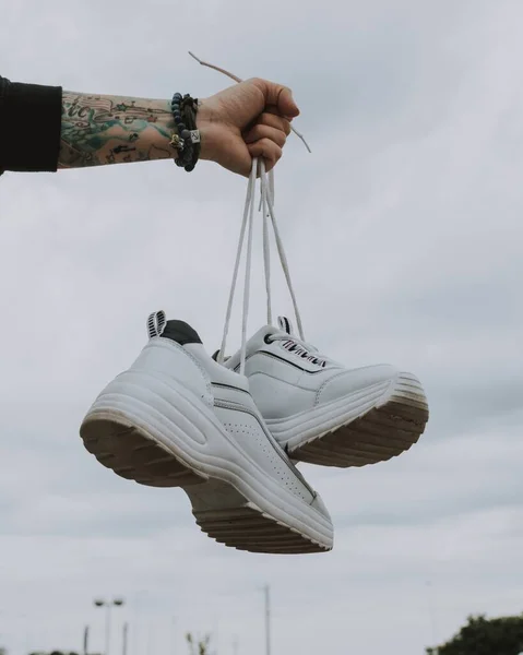 Vertical shot of a person holding from the laces of white sports shoes — 스톡 사진