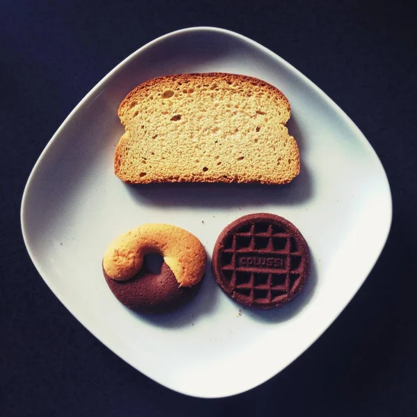Tiro de alto ângulo de pão torrado, donut e chocolate em uma placa de cerâmica branca — Fotografia de Stock
