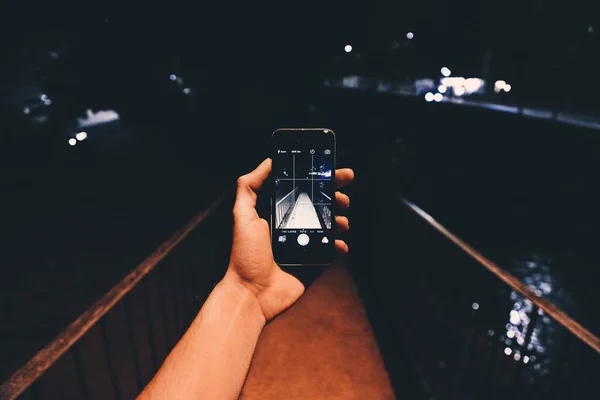 Az okostelefonnal rendelkező személy éjszaka fényképet készít a tó feletti hídról — Stock Fotó