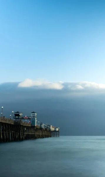 Pionowe ujęcie molo obok akwenu wodnego z gęstymi chmurami na niebie — Zdjęcie stockowe