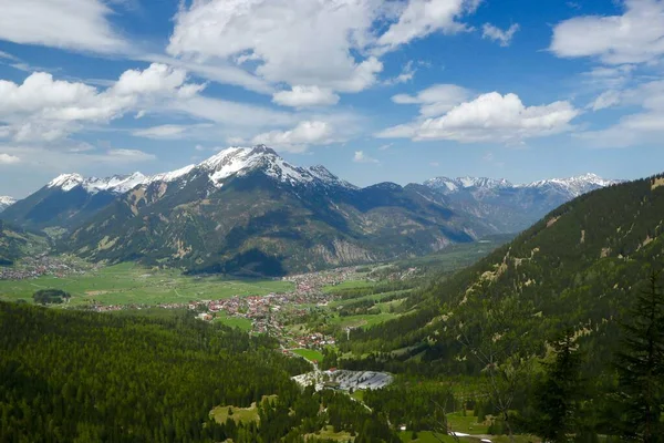 Weitwinkelaufnahme einer wunderschönen, mit Schnee und grünen Bäumen bedeckten Gebirgskette unter dem wolkenverhangenen Himmel — Stockfoto