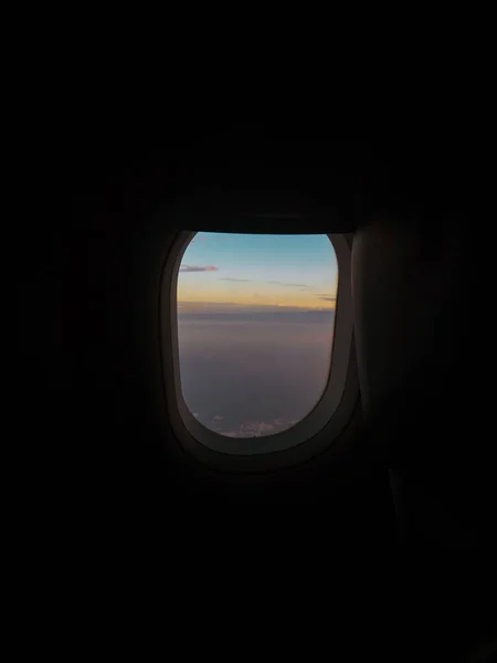 Captura vertical de una ventana de avión con la vista de las nubes y un cielo azul — Foto de Stock