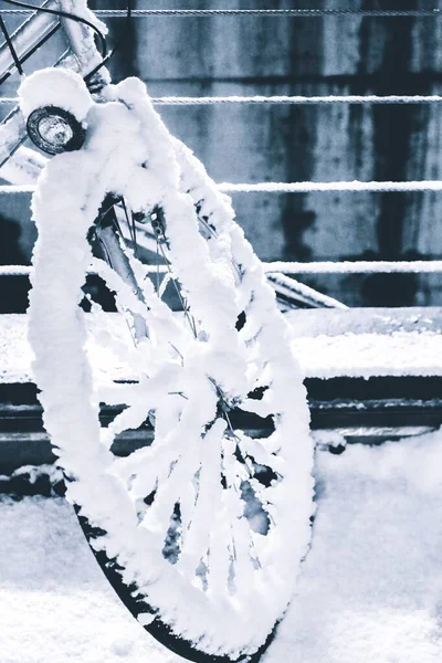 Verticale opname van een fietswiel bedekt met sneeuw in de buurt van metalen leuningen — Stockfoto