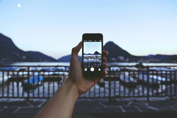 Persona con un smartphone tomando una foto de la impresionante vista con montañas y barcos — Foto de Stock