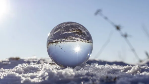 Close-up shot van een glazen bal op sneeuw die de grond en de zon reflecteert. Perfect voor een behang — Stockfoto