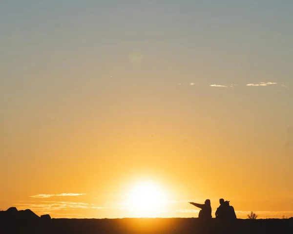 Plan horizontal de deux personnes en silhouette assises sur le sol au coucher du soleil — Photo