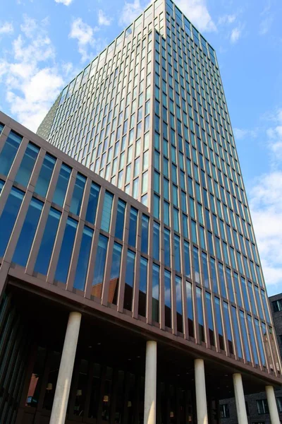 Tiro vertical de um edifício alto com janelas de espelho sob o belo céu nublado na Alemanha — Fotografia de Stock