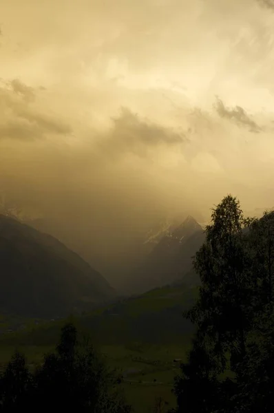 Tiro vertical de colinas cubiertas de hierba cerca de las montañas bajo un cielo nublado y nebuloso — Foto de Stock