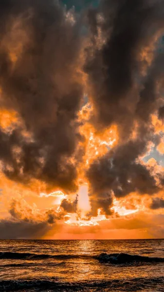 Vertikale Aufnahme eines wunderschönen Meeres mit der Reflexion der atemberaubenden Wolken, die wie ein Feuer aussehen — Stockfoto