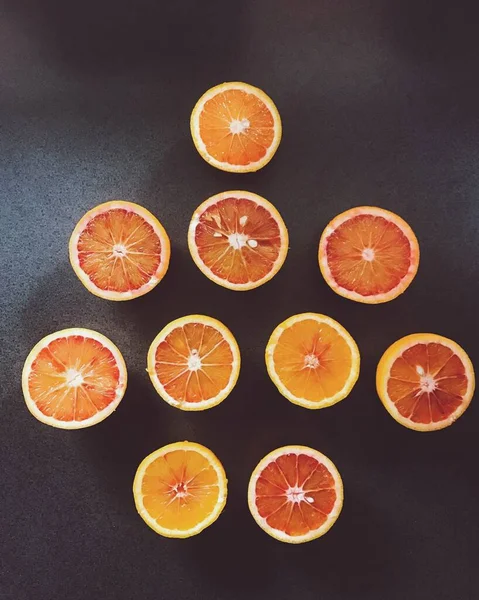 Tiro vertical de alto ángulo de naranjas en rodajas sobre una superficie negra, ideal para un fondo de pantalla creativo — Foto de Stock