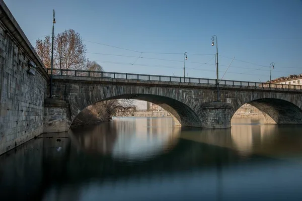 Poziome ujęcie betonowego mostu z łukami nad wodą w Turynie, Włochy pod błękitnym niebem — Zdjęcie stockowe