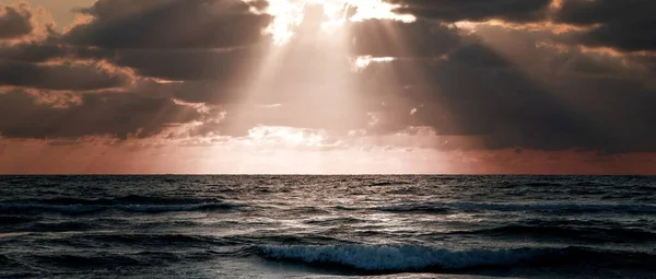 白い雲の中から美しい太陽の光が差し込む波の海の美しいワイドショット — ストック写真