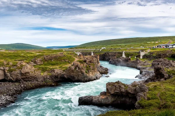 Un río de Godafoss Falls, Akureyri, Islandia, rodeado de enormes rocas y un puente de hormigón — Foto de Stock