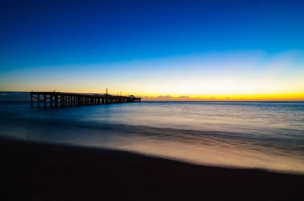 Hermosa puesta de sol sobre el mar azul marino con un gran puente bajo el cielo azul claro brillante — Foto de Stock