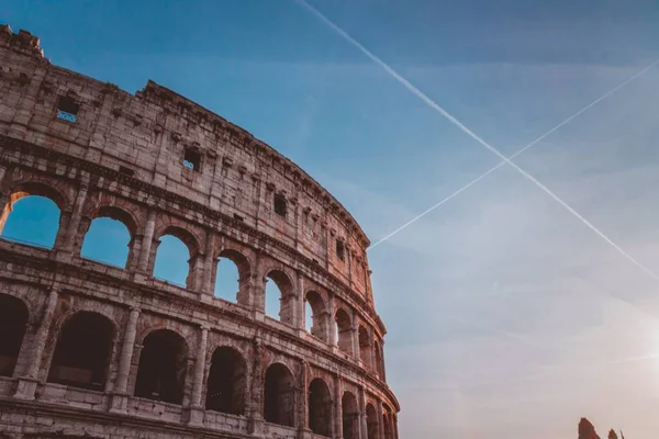 青い空に飛行機の痕跡の背景とローマ、イタリアのコロッセオの低角度ショット — ストック写真