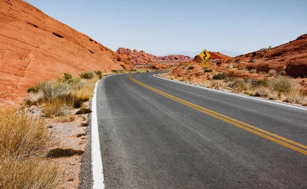 Vodorovný záběr na prázdnou dálnici uprostřed červené skalnaté pouště, se znakem vedle silnice. — Stock fotografie
