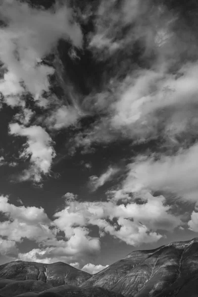 Scala di grigi caldo di belle nuvole bianche sotto il cielo limpido e montagne rocciose a Norcia, Italia — Foto Stock