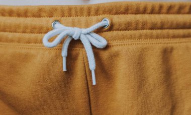 Selective closeup shot of the white tied laces of brown sweatpants clipart