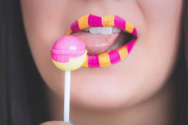 Horisontell närbild bild av en kvinna med ett gult och rosa läppstift äter en klubba — Stockfoto