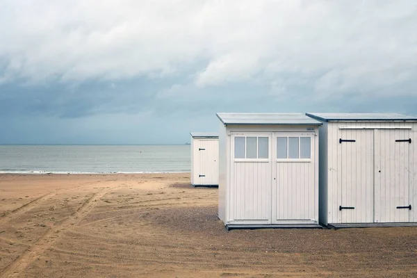 Hermosa toma de pequeñas habitaciones blancas en una playa cerca del agua bajo un cielo nublado — Foto de Stock