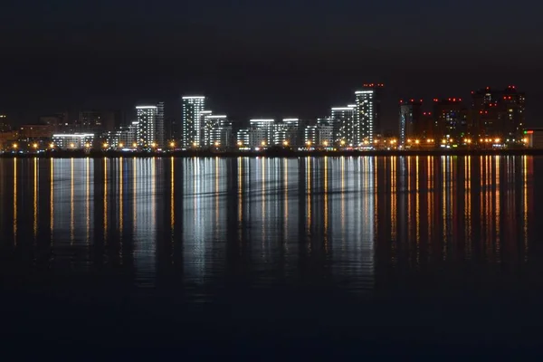 Vue d'ensemble de hauts bâtiments avec des lumières réfléchies dans l'eau sous le beau ciel nocturne — Photo