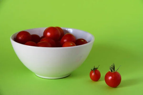 Close shot of small tomatoes in a white bowl on a green surface — Stock Photo, Image